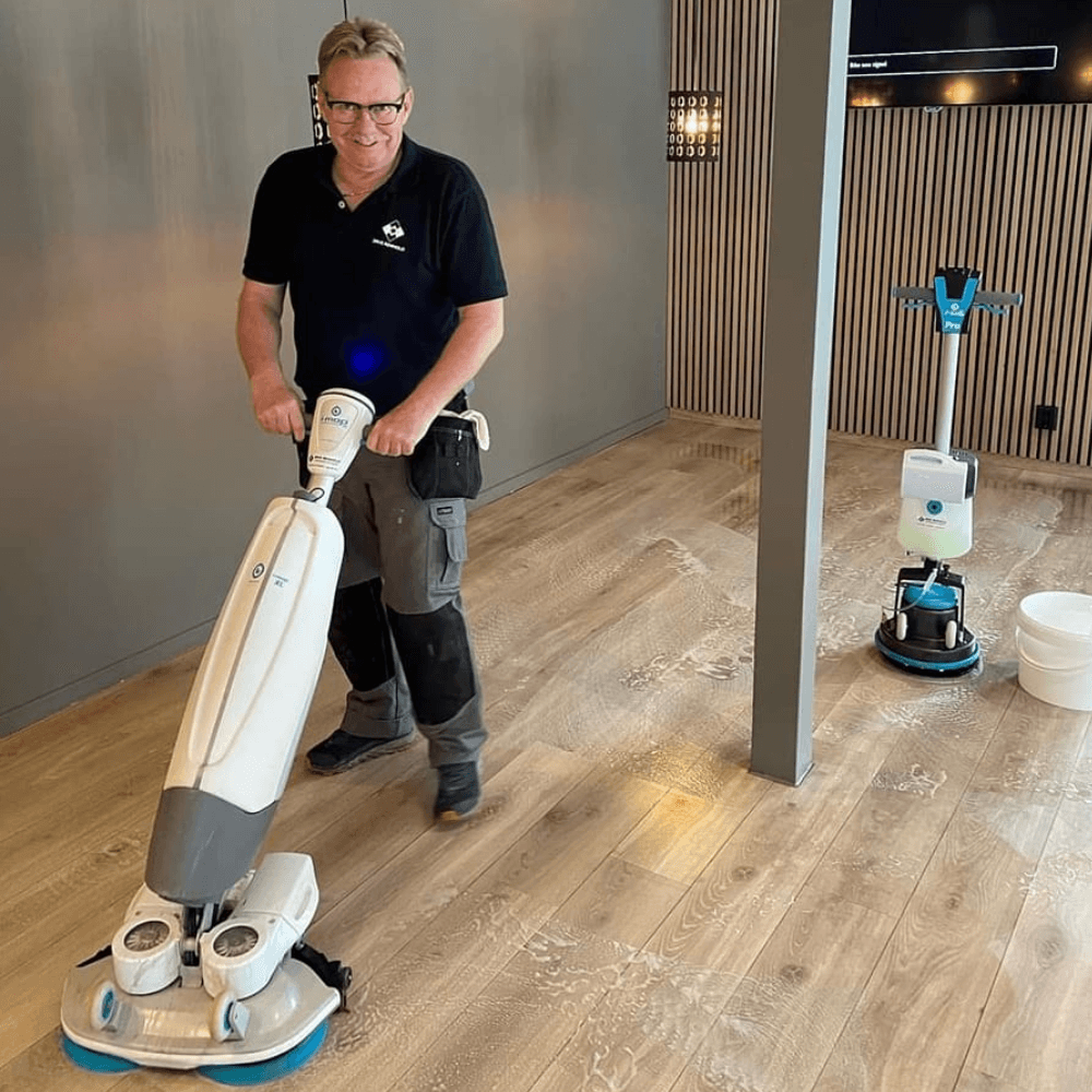 Medarbeider som skurer et tregulv med gulvmaskin
